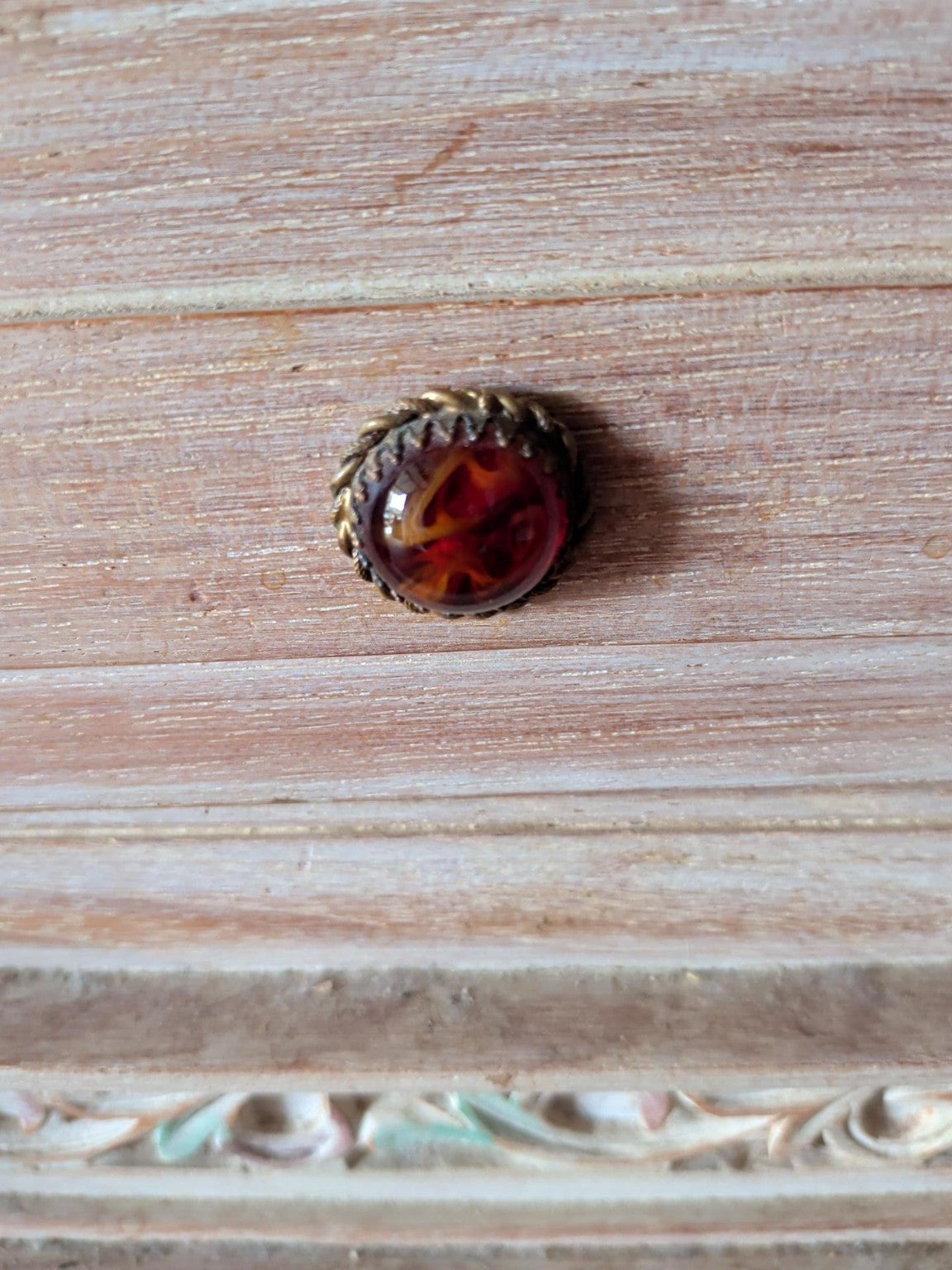 Close-up of amber-effect decorative drawer knob with ornate metal-effect surround on actual cabinet