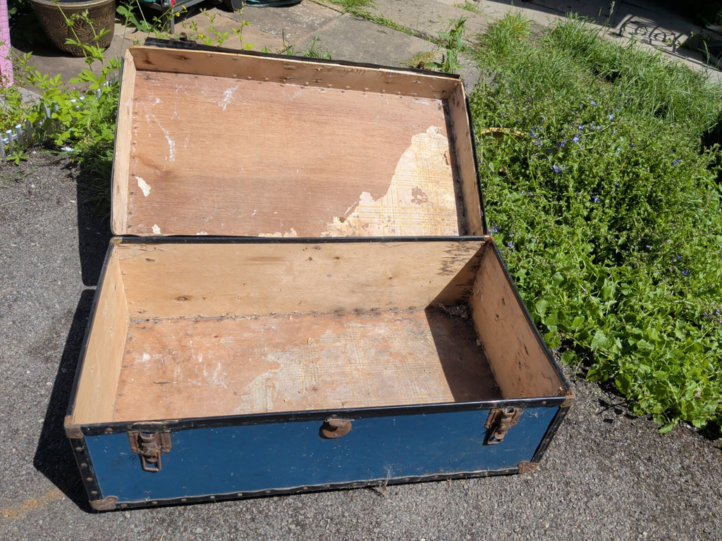 Open vintage blue travel trunk showing wooden interior and aged lining
